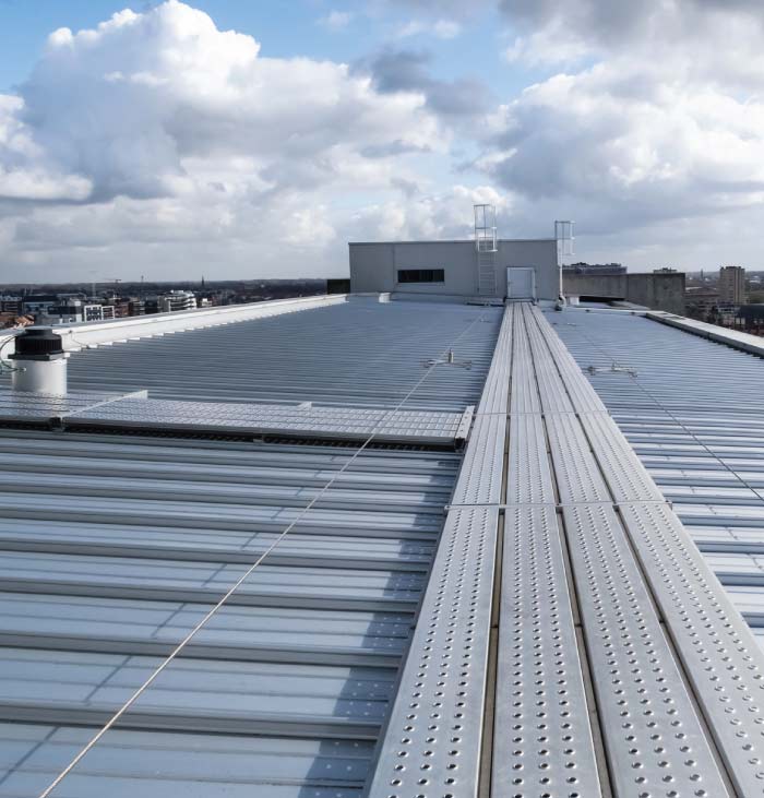 Quality-metal-Roofing-Services- Professional shot of a commercial metal roof featuring a walkway system, ventilation vents, safety lines, and a rooftop access structure under blue skies.