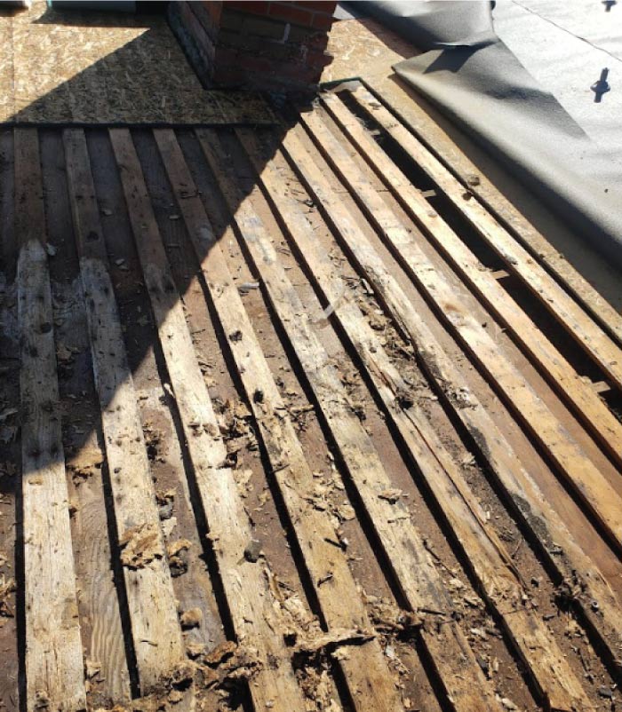 Old, damaged wooden skip sheathing roof deck exposed after removing the existing roofing materials, showing wear and debris requiring dry-rot replacement.