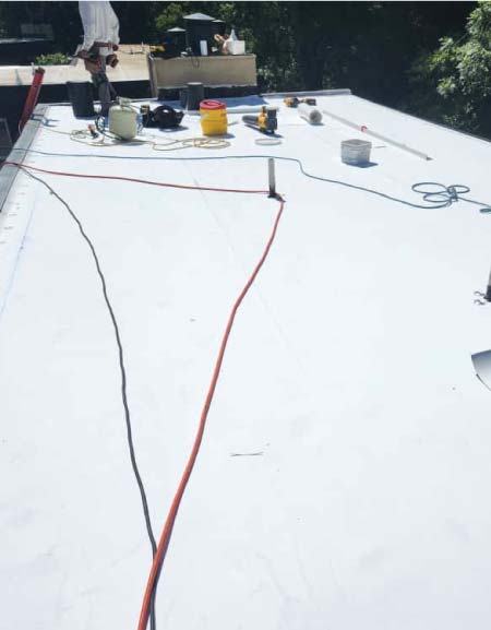 metal-roof A white, flat TPO membrane roof installation in progress with tools, power cords, and equipment visible on a sunny day.