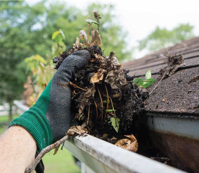 A downspout clogged with leaves and debris overflowing A clogged downspout overflowing onto a damaged foundation.