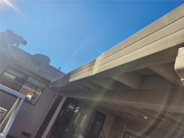 Looking up at a damaged and sagging metal gutter on a residential home, highlighting the need for professional gutter and downspout installation to prevent structural water damage.