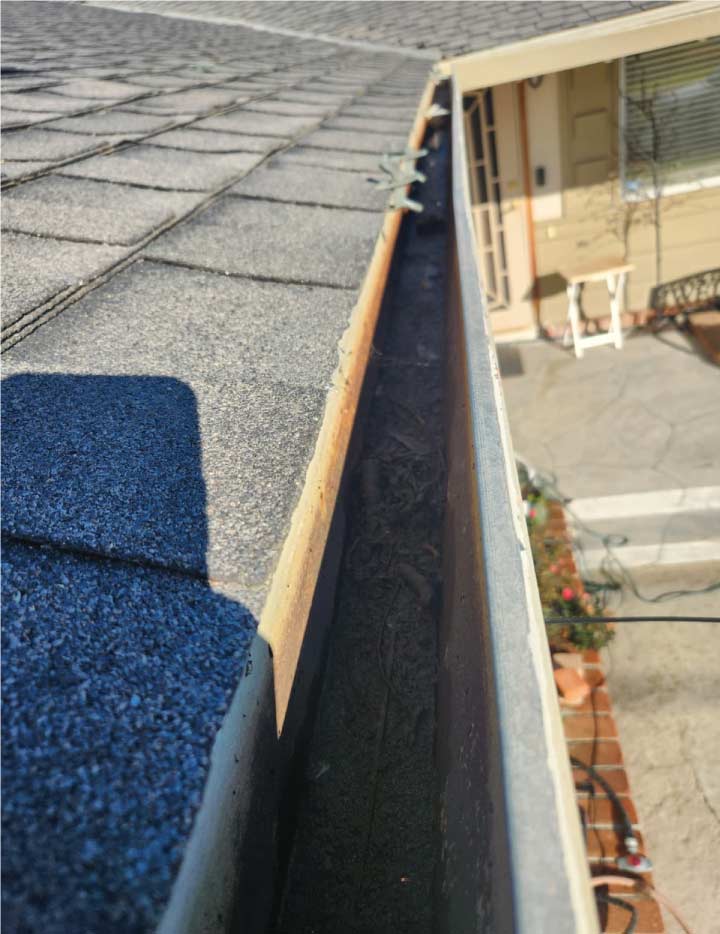 Close-up of a professionally cleaned residential gutter in Antioch, CA, showing a clear, debris-free channel along a dark shingle roof edge to ensure proper water drainage.