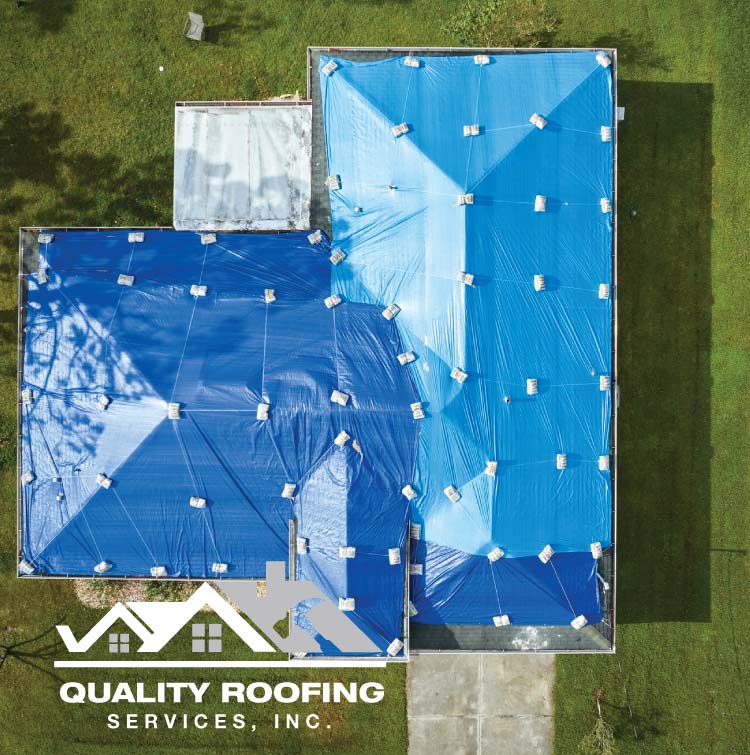 Aerial view of a large residential home in Antioch, CA receiving professional roof tarping services with heavy-duty blue tarps secured by weights to prevent interior water damage after a major storm.