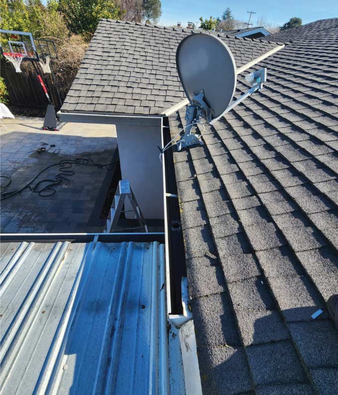 High-angle view of a grey shingle roof with a satellite dish and a perfectly maintained gutter system, illustrating a successful gutter cleaning service performed by Quality Roofing Services, Inc